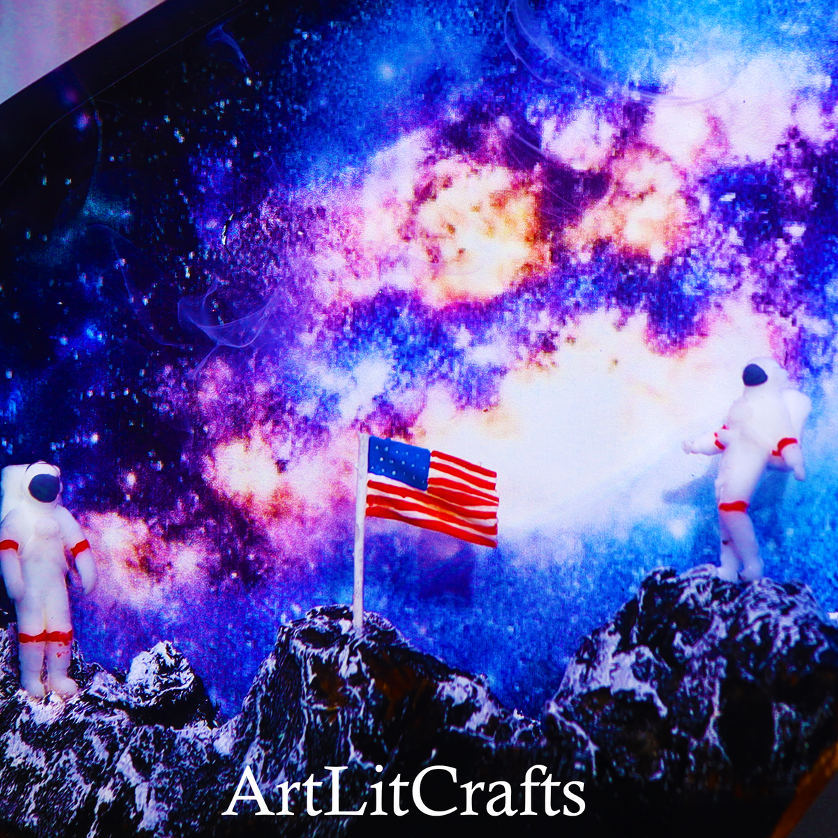 Two astronauts on a moon surface with an American flag, set against a colorful space background. Brand 'ArtLitCrafts' visible.