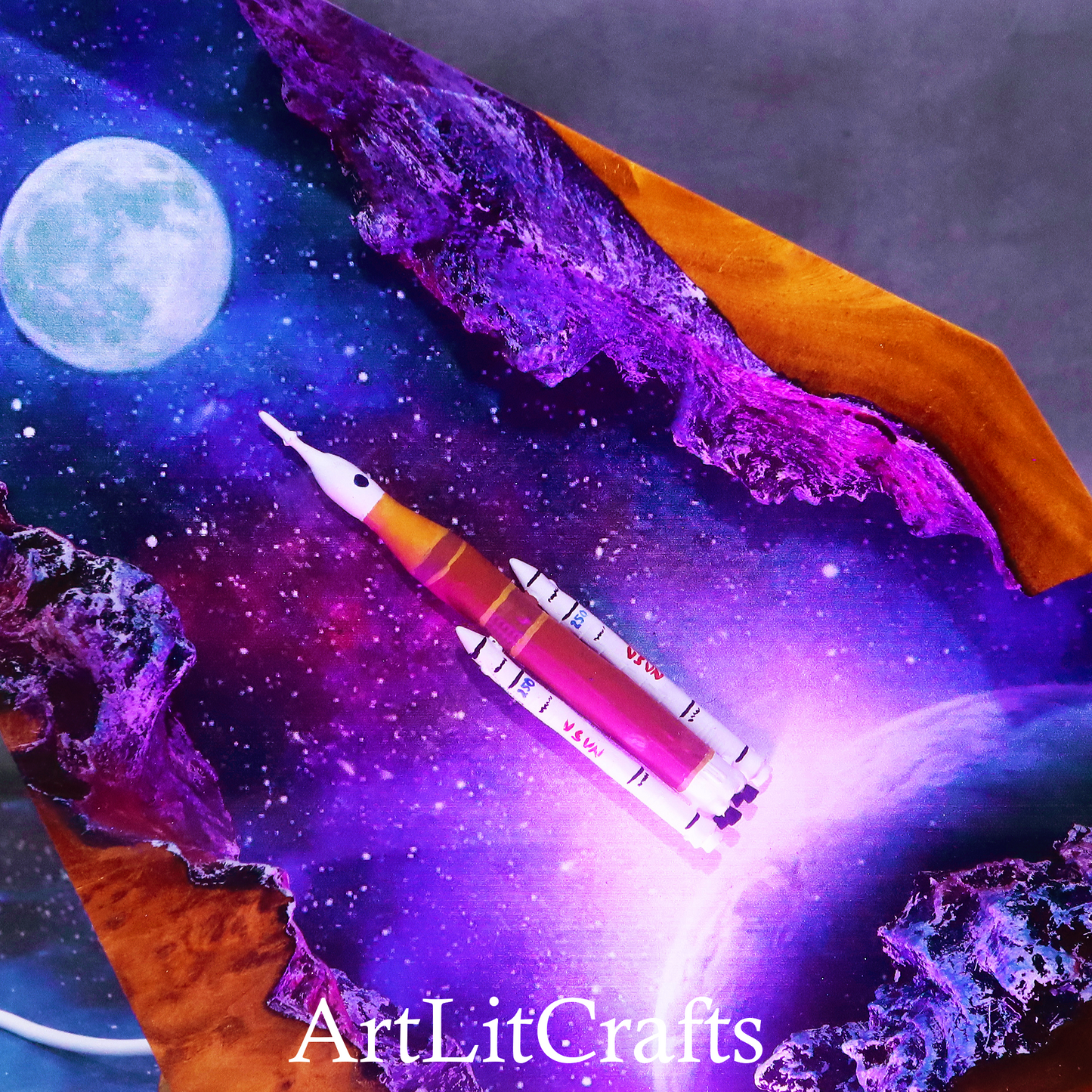 Close up galaxy resin lamp glowing with purple ambient lighting, featuring the brand 'ArtLitCrafts'.