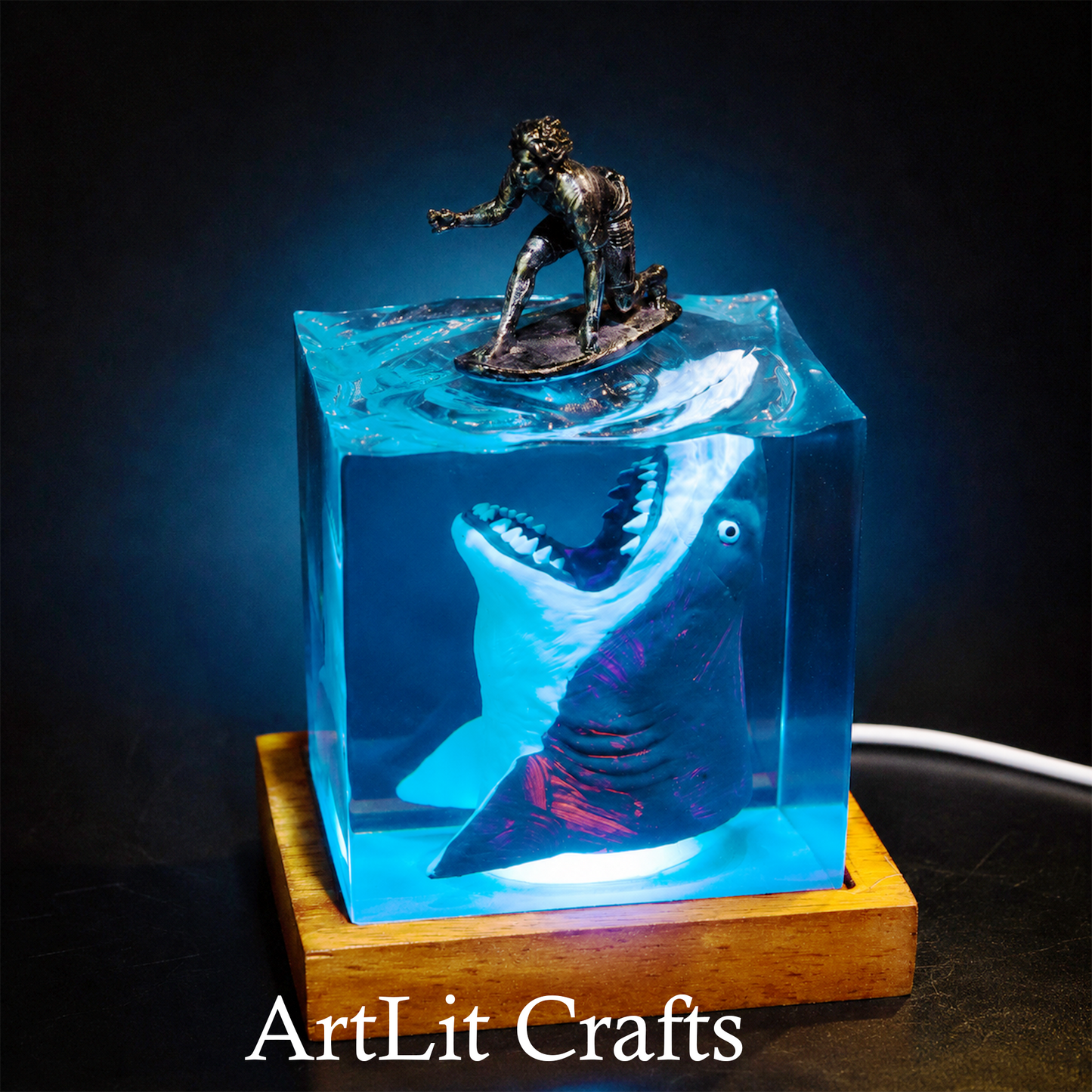 Decorative piece with a shark and figure inside a transparent resin lamp on a wooden base, illuminated with blue light.